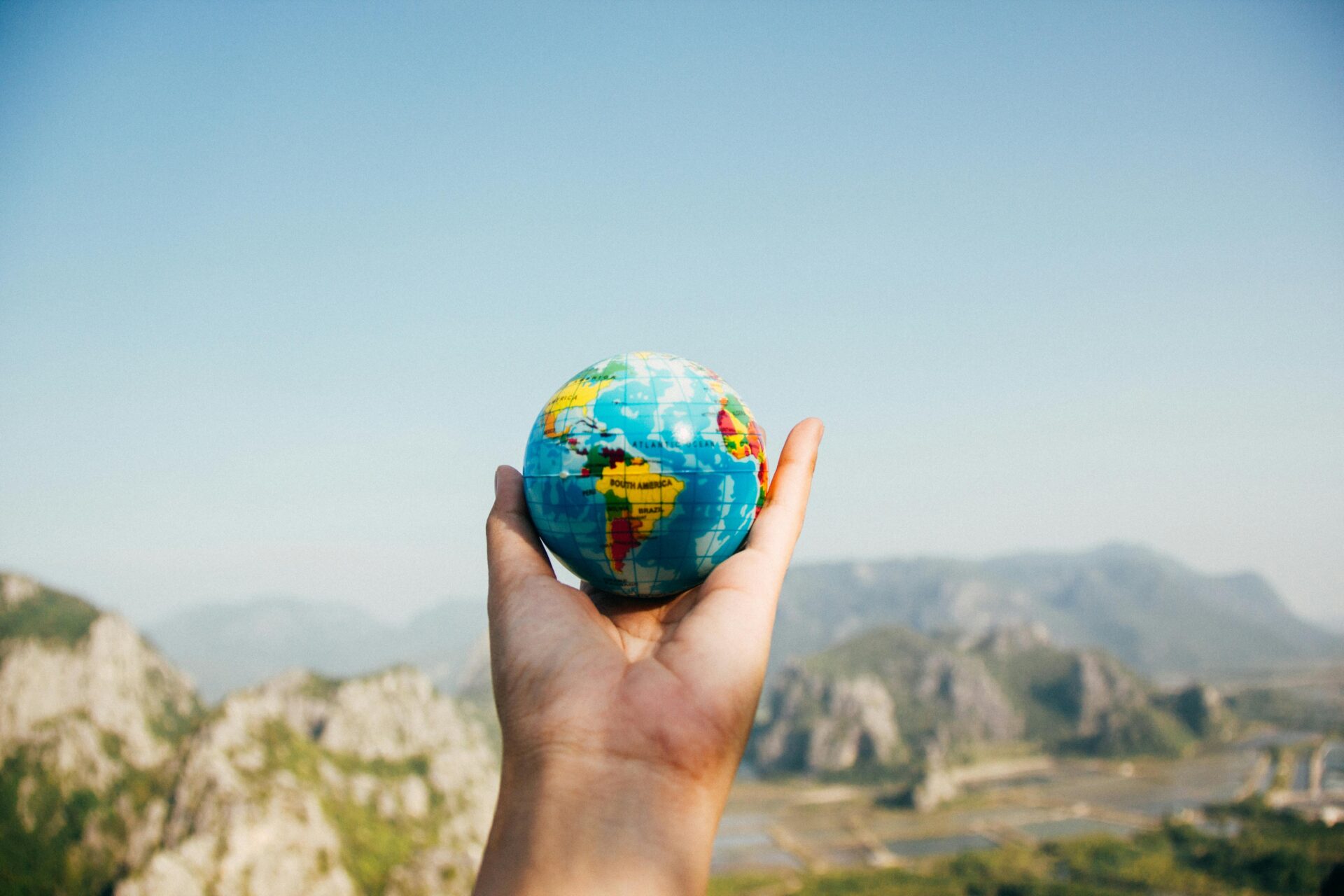 Person holding world globe facing mountain